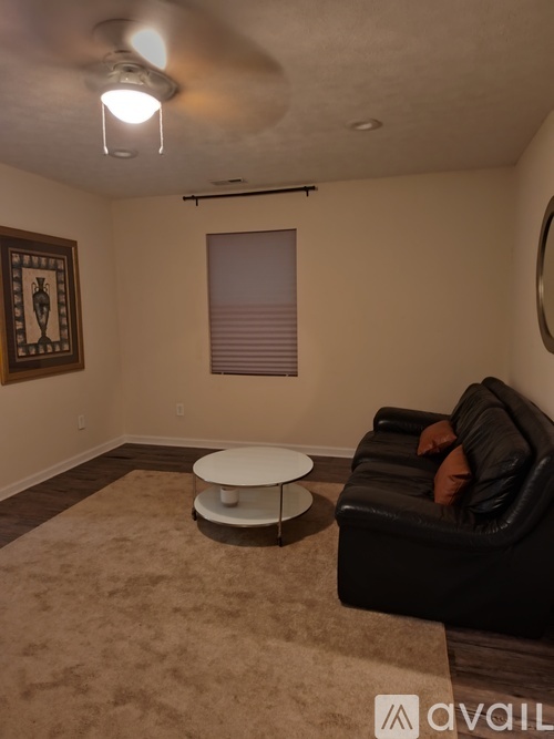 A living room with a black couch, a round table, and a framed picture on the wall.