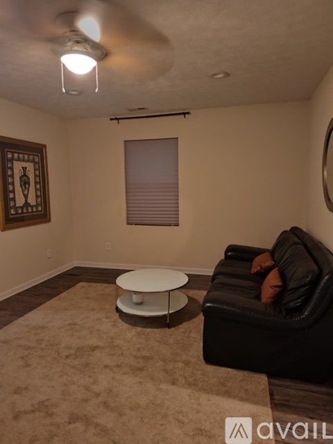A living room with a black couch, a round table, and a framed picture on the wall.