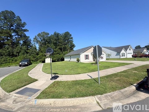 A basketball hoop is in the middle of a grassy area in front of a house.