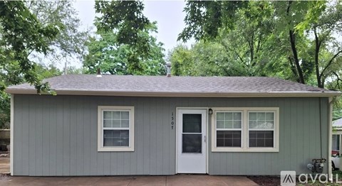A small house with a white door and windows is surrounded by trees.