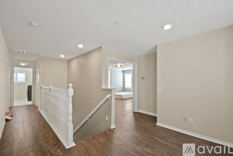 A spacious room with wooden floors and a staircase with white railings.
