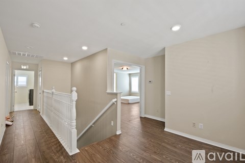 A spacious room with wooden floors and a staircase with white railings.