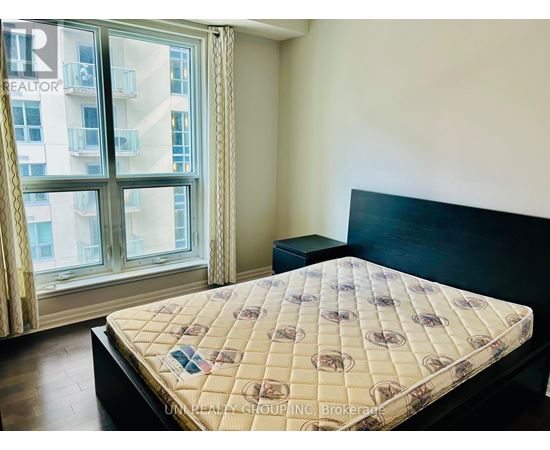 A bed with a patterned cover sits in a room with a large window.