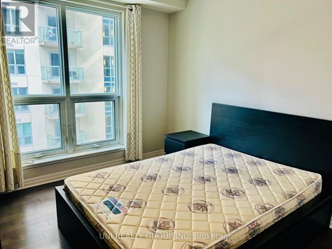 A bed with a patterned cover sits in a room with a large window.