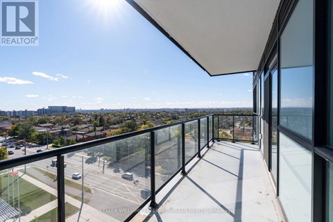 A balcony with glass railings overlooks a parking lot and buildings.