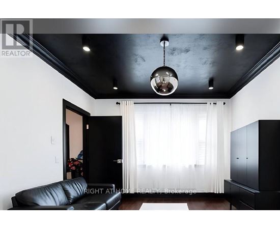 A black leather sofa sits in a room with a black ceiling and a chandelier hanging from it.