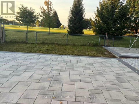 A paved walkway leads to a grassy area with a fence.