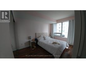 A bedroom with a white bed and a window with white curtains.