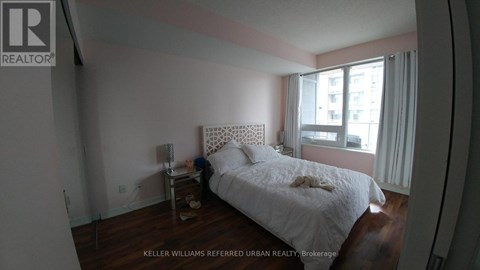 A bedroom with a white bed and a window with white curtains.