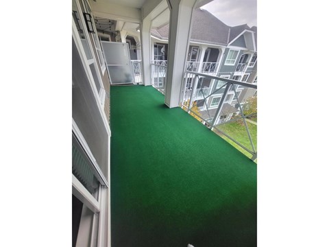 A green carpeted hallway with white railings and a white building in the background.