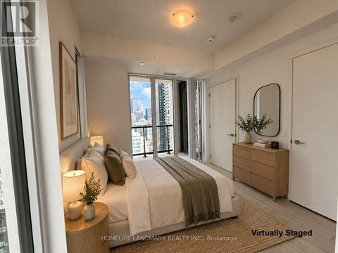 A bedroom with a bed, nightstand, and a window with a view of the city.