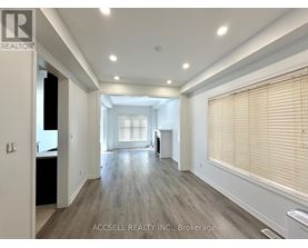 A spacious room with wooden flooring and a large window with blinds.