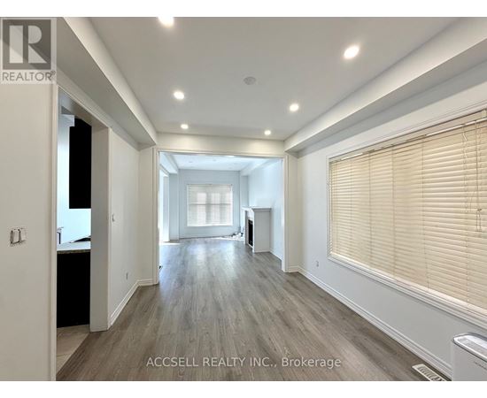 A spacious room with wooden flooring and a large window with blinds.