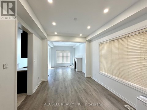 A spacious room with wooden flooring and a large window with blinds.