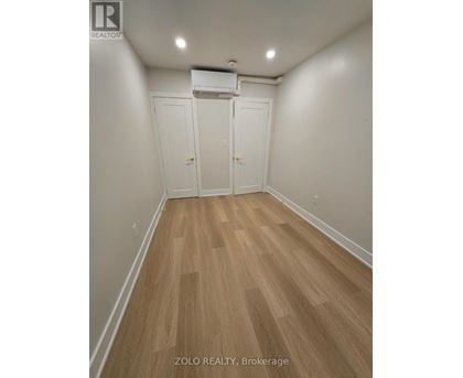 A room with wood flooring and white walls, with a white air conditioner unit on the wall.