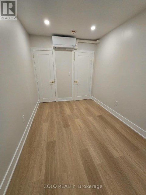 A room with wood flooring and white walls, with a white air conditioner unit on the wall.