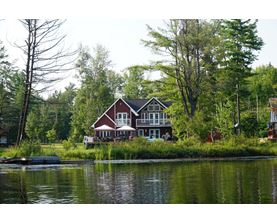 A house with a red roof is situated by a body of water.