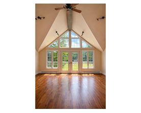 A room with a ceiling fan and a large window with a view of trees.
