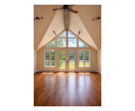 A room with a ceiling fan and a large window with a view of trees.
