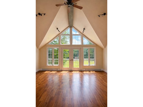 A room with a ceiling fan and a large window with a view of trees.