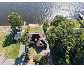A house with a brown roof is surrounded by trees and is located near a body of water.