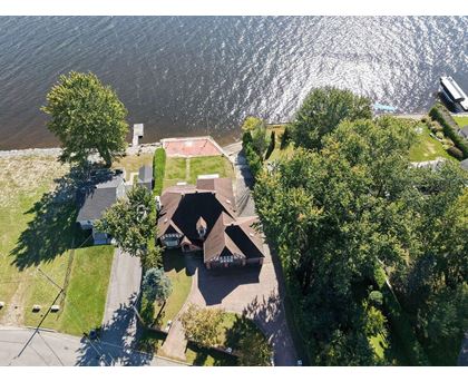 A house with a brown roof is surrounded by trees and is located near a body of water.