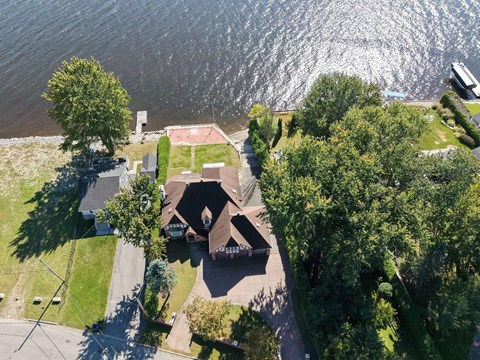 A house with a brown roof is surrounded by trees and is located near a body of water.