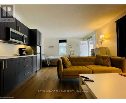A living room with a yellow couch and a kitchen area with black cabinets.