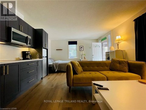 A living room with a yellow couch and a kitchen area with black cabinets.