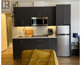 A kitchen with black cabinets and a stainless steel refrigerator.