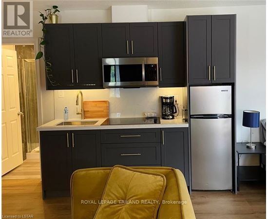 A kitchen with black cabinets and a stainless steel refrigerator.