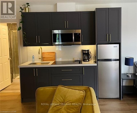 A kitchen with black cabinets and a stainless steel refrigerator.