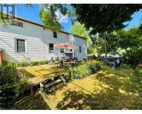 A backyard with a white house, a patio with chairs and a table, and a few people sitting.