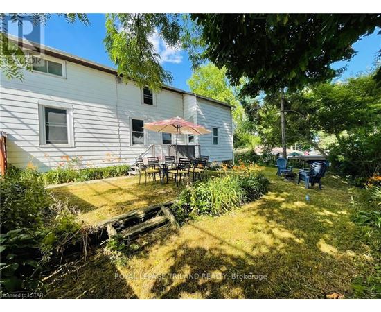 A backyard with a white house, a patio with chairs and a table, and a few people sitting.