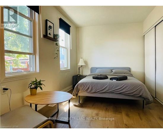 A bedroom with a bed, nightstand, and a table with a plant on it.