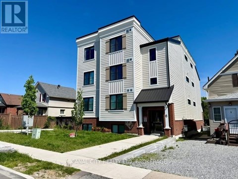A modern two-story building with a balcony on the second floor is surrounded by other houses.