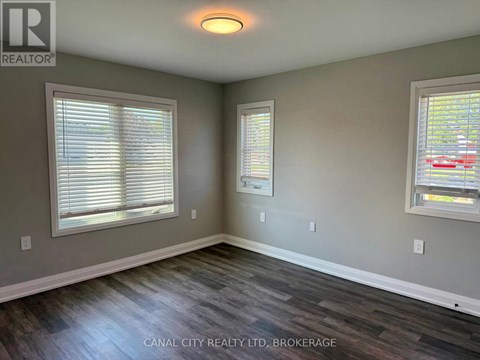 A room with wood flooring and two windows.