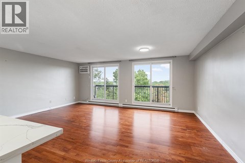 A spacious room with wooden flooring and a sliding glass door leading to a balcony.