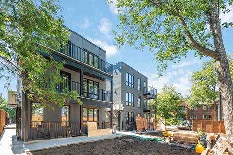 A modern two-story building with a balcony and a tree in front.