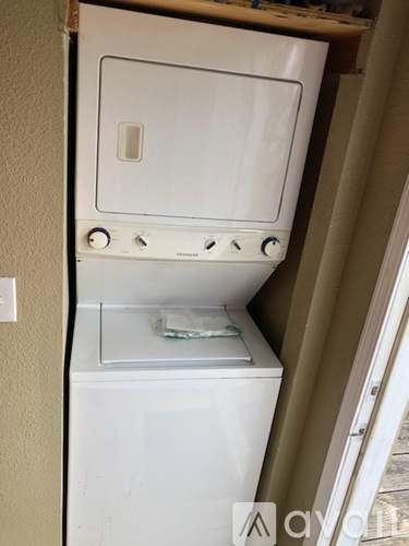 A white dishwasher is sitting in a narrow space between a wall and a door.