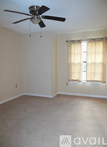A room with a ceiling fan and a window with curtains.