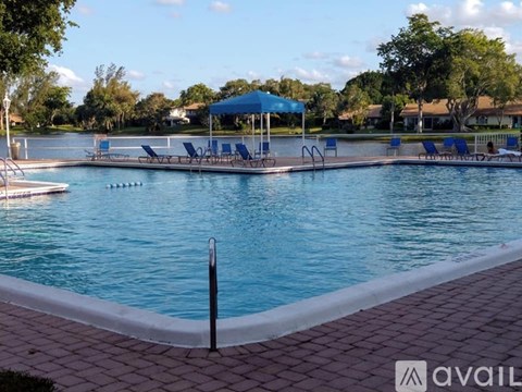 A pool with blue water and a white edge with a blue umbrella in the background.