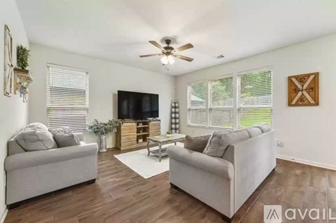 A living room with a grey couch, a white couch, a wooden entertainment center, and a ceiling fan.