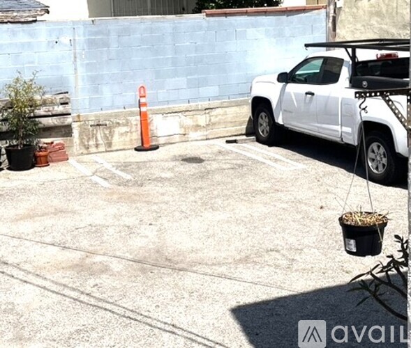 A white truck is parked in a lot with a plant in a black pot hanging from a hook.