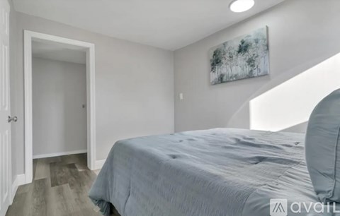 A bedroom with a bed, a painting on the wall, and a doorway leading to another room.