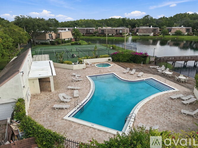 A pool surrounded by chairs and a tennis court in the background.
