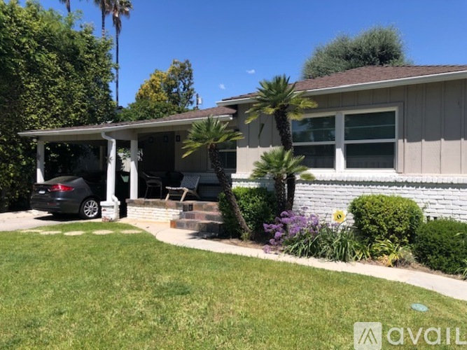 A house with a car parked in front and a palm tree in the front yard.