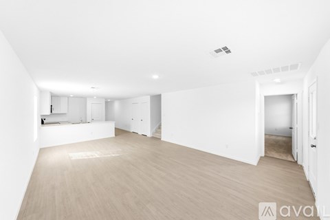 A spacious, empty room with wooden flooring and white walls.