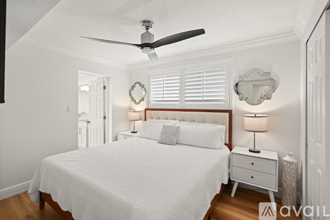 A bedroom with a white bed, a ceiling fan, and a nightstand with a lamp.
