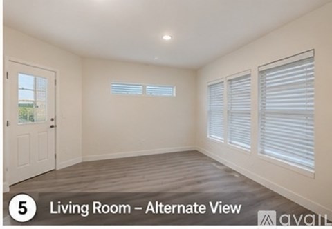 A living room with a door, two windows with blinds, and a wooden floor.